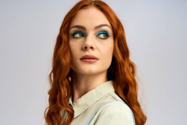 Genç bir kızıl, canlı makyaj ve büyüleyici bir stil sergileyerek kendine güvenen bir şekilde stüdyoda poz veriyor..