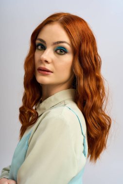 Genç kızıl saçlı bir kadın stüdyoda zarif poz verirken göz makyajı yapıyor..