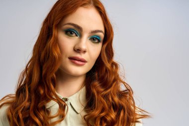 Göz alıcı kızıl saçlı genç bir kadın yaratıcı stüdyo sahnesinde cesur göz makyajı sergiliyor..