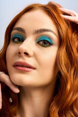 Göz alıcı makyajlı genç kızıl saçlı zarif bir şekilde parlak bir stüdyoda poz veriyor ve güzelliği vurguluyor..
