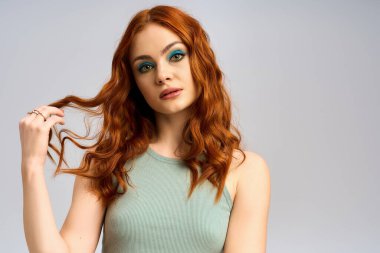 Canlı kızıl saçlı genç bir kadın sanatsal makyajını stüdyoda sergiliyor..