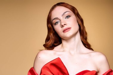 Genç kızıl saçlı bir kadın zarif bir şekilde poz veriyor, canlı kırmızı bir yayla bayram neşesini sunuyor..