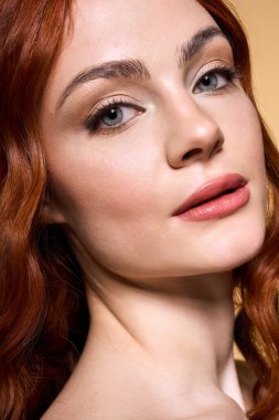 Genç kızıl, yumuşak makyajlı ve parlak tenli bir stüdyoda zarif pozlar veriyor..