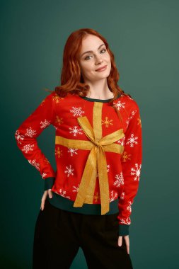 Noel süveteri giymiş neşeli bir kızıl yeşil bir fonda poz verir..