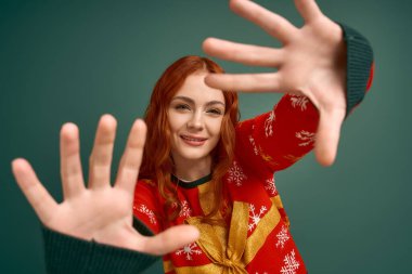 Kızıl saçlı genç bir kadın Noel süveteri içinde neşeli pozlar veriyor, bayram ruhunu kutluyor..