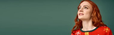 Noel süveteri içinde şenlikli bir şekilde, genç kızıl saçlı bir kadın yeşil bir arka fona gülümsüyor, afiş.