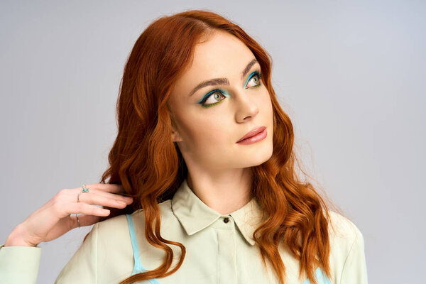 Молодая рыжая демонстрирует смелый, красочный макияж, позируя в яркой студии.