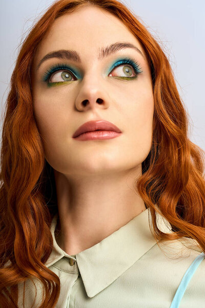 Молодая женщина с рыжими волосами и поразительным макияжем глаз изящно позирует в студии.