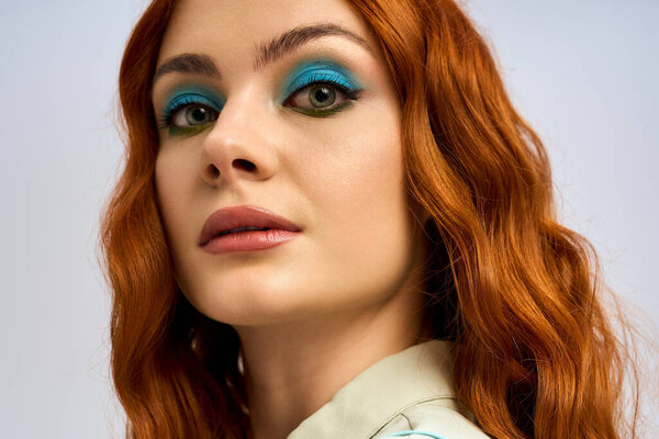 Молодая рыжая с ярким макияжем позирует в яркой студии, излучая уверенность и артистизм.