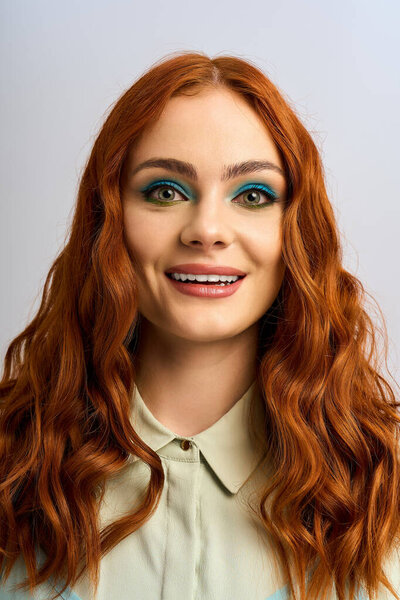 Молодая рыжая рыжая с ярким макияжем для глаз счастливо позирует в студии.