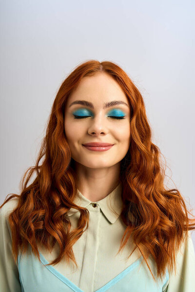Молодая женщина с яркими рыжими волосами демонстрирует яркие синие глаза макияж в стильной студии.