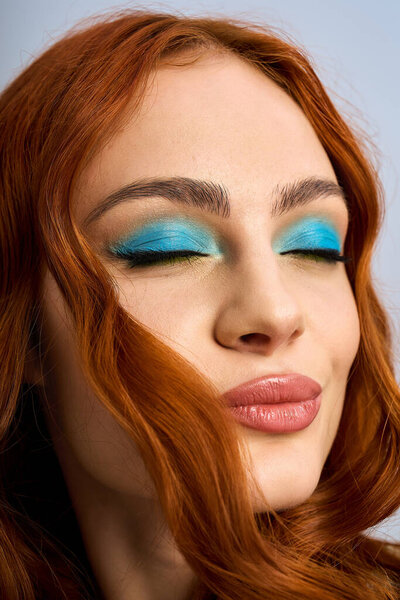 Young woman with stunning red hair poses confidently in a studio, showcasing vibrant makeup.