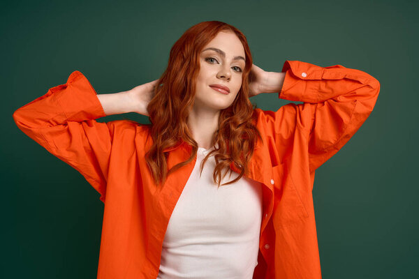 A redhead in an orange shirt smiles confidently against a green backdrop this autumn.