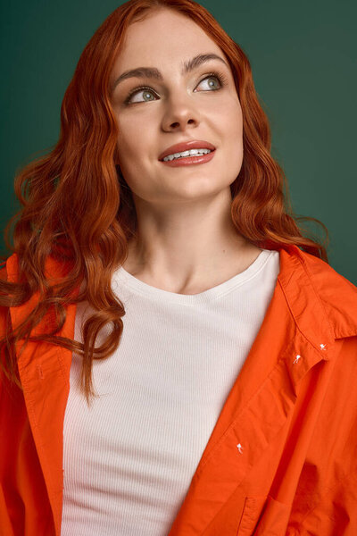 Молодая рыжая женщина моделирует оранжевую рубашку, источая осенний стиль с радостным выражением лица.