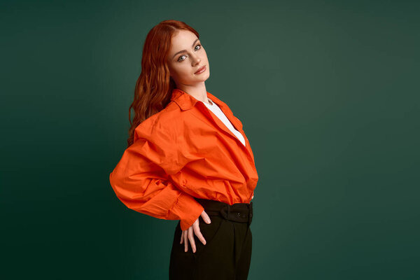 Уверенный рыжий в оранжевой рубашке позирует на фоне зеленого задника, демонстрируя осенний стиль.