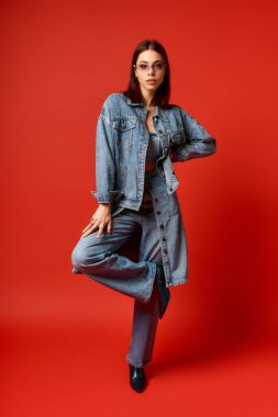 Modayı takip eden genç bir kadın kırmızı duvarları olan bir stüdyoda kot tarzını sergiliyor..