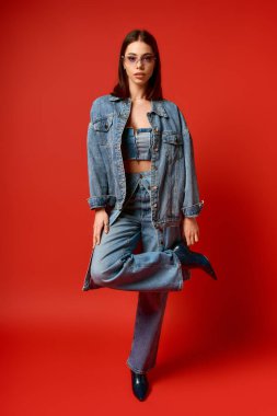 Kot ceket ve kot pantolonla poz veren genç bir kadın stüdyoda kendine güveni ve tarzı yayıyor..
