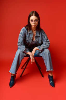 Genç bir kadın, canlı kırmızı bir arka planda kot giyip güvenle poz veriyor..