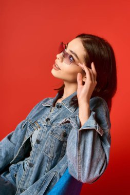 Şık bir genç kadın kot ceket ve kotla rahatça poz verir. Stüdyoda göz kamaştırıcı bir çekiciliği vardır..