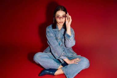 Kot ceketli ve kot pantolonlu genç bir kadın stüdyoda şık poz veriyor..