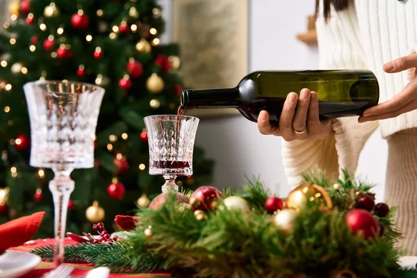 Celebrando o Natal com os amigos, derramando vinho tinto ao lado de uma árvore lindamente decorada — Fotografia de Stock