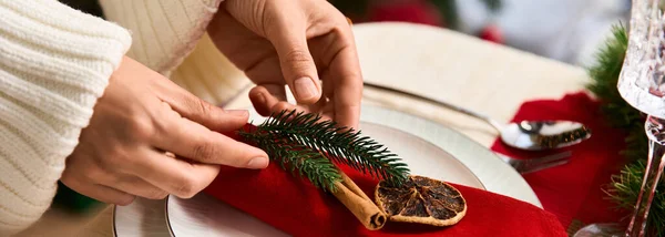 Mãos arranjar um guardanapo vermelho com canela e vegetação para uma refeição de Natal alegre. — Fotografia de Stock