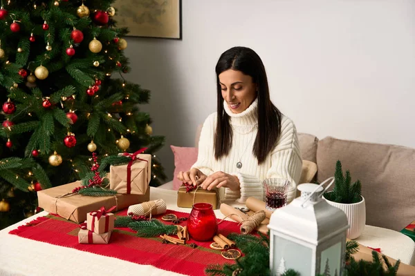Uma mulher envolve presentes alegremente ao lado de uma árvore de Natal lindamente decorada. — Fotografia de Stock