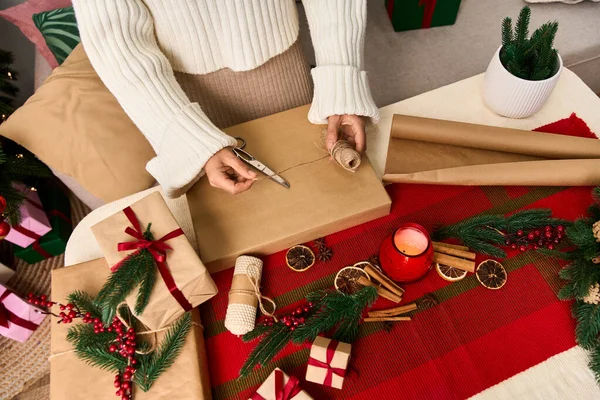 Una persona envuelve cuidadosamente un regalo con papel marrón, rodeado de decoraciones festivas y plantas. - foto de stock