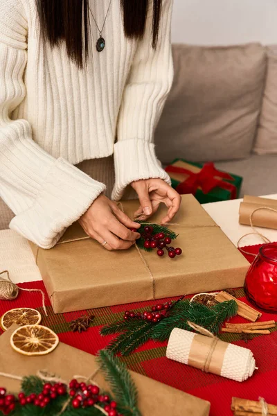 A pessoa decora cuidadosamente um presente com acentos naturais e cores de férias em uma mesa aconchegante. — Fotografia de Stock
