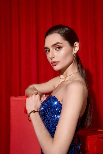 Junge Frau in festlichem Gewand posiert freudig vor leuchtend roter Kulisse. — Stockfoto