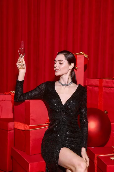 Молода жінка елегантно позує у святковому одязі, радісно святкуючи серед червоних прикрас та подарунків. — стокове фото