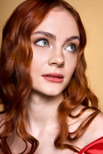 Una joven pelirroja exhibe su llamativo maquillaje mientras posa en un ambiente de estudio brillante. - foto de stock