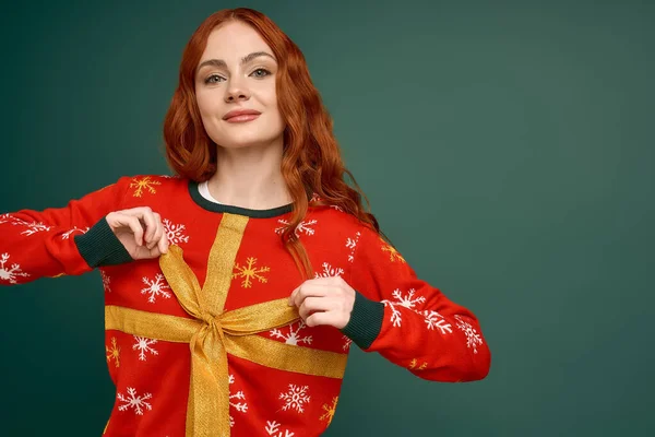 A cheerful young woman proudly wears her Christmas sweater with a big bow, excited for the holidays. — Stock Photo