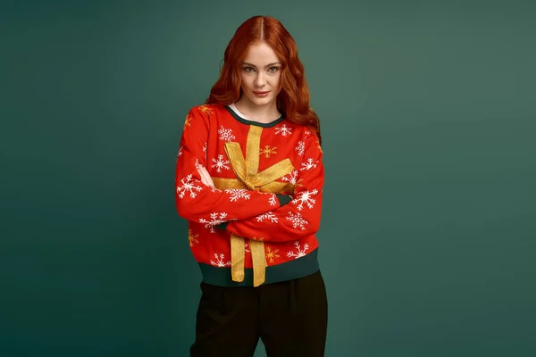 Eine fröhliche junge Frau mit roten Haaren trägt einen stylischen Weihnachtspullover und umarmt die Feiertagsstimmung. — Stockfoto