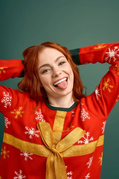 Uma jovem mulher com cabelo vermelho posa em uma camisola de Natal colorida contra um pano de fundo verde. — Fotografia de Stock