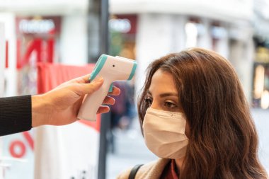 Covid-19 salgını sırasında süpermarketten alışveriş yapmadan önce koruyucu maske takan müşterilerin termometresi termometreyi kontrol ediyor. Yeni normal yaşam tarzı kavramı.