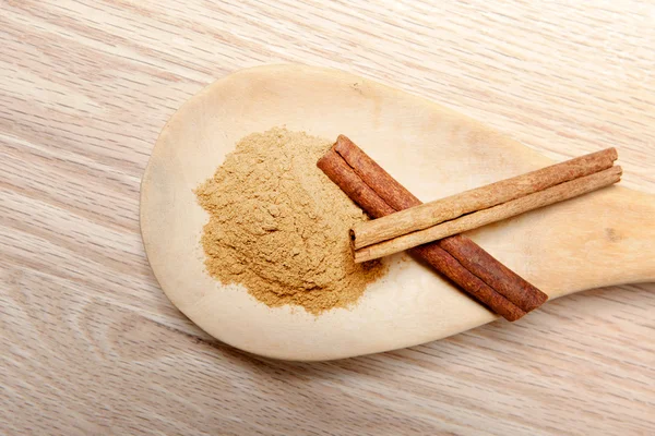 Paus de canela e pó de canela em uma colher de madeira — Fotografia de Stock