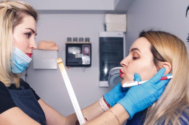 Güzellik uzmanı dudakları kalıcı makyaj için hazırlar, model aynaya bakar..