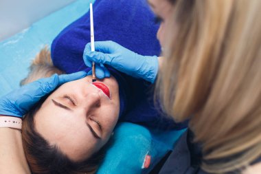 Güzellik uzmanı dudakları kalıcı makyaj için hazırlar, model aynaya bakar..