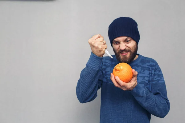 an angry bearded man wants to cut out the navel of an orange with a scalpel. concept of problems due to hemorrhoids