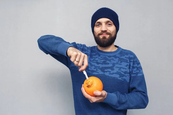 a cheerful bearded man wants to cut out a large navel of an orange with a scalpel, the concept of hemorrhoids or proctological diseases