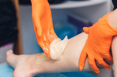 Kadın kozmetik uzmanı spa salonunda şeker ezmesiyle çalışıyor. Şeker macunuyla yakın plan saç kesimi..