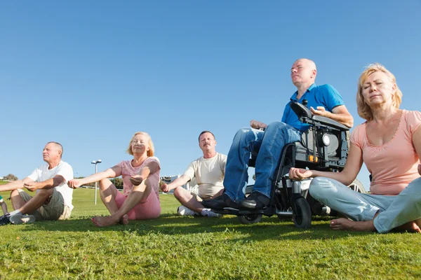 Behinderter Mann mit Familie praktiziert draußen Yoga. — Stockfoto
