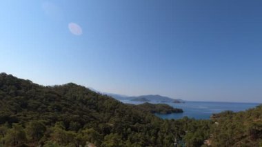 Dağların ve denizin panoramik manzarası. Parlak yaz güneşi sıcak ışınlarla parlıyor. Gökyüzü açık ve mavi.