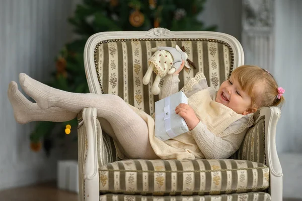 Little funny girl having fun in a chair in front of Christmas tree — Stock Photo, Image