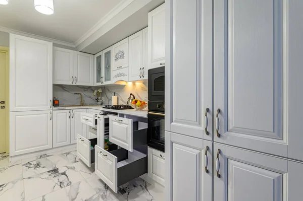 Open drawers with kitchenware at modern white kitchen