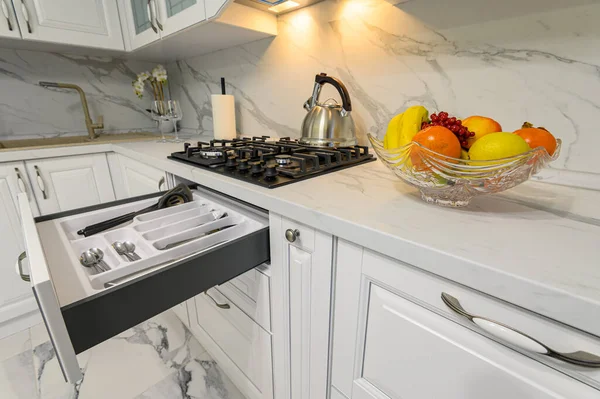 Open drawers with kitchenware at modern white kitchen