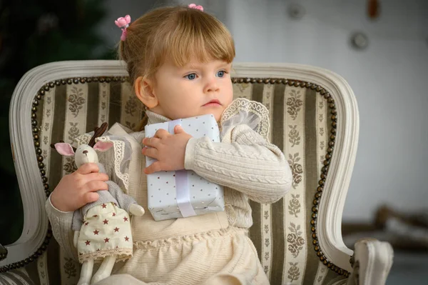 Niña rubia se sienta en una silla frente al árbol de Navidad — Foto de Stock