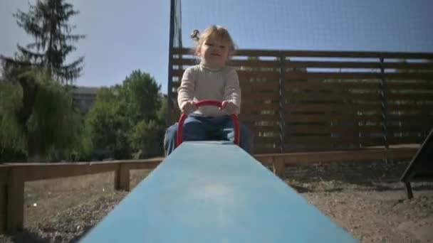 Kis aranyos szőke lány lovagol teeter Totter a játszótéren — Stock videók