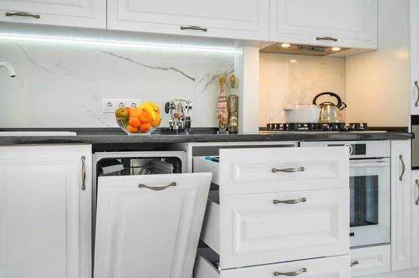 Luxusní bílý moderní kuchyňský interiér, vytažené zásuvky, otevřené dveře od myček nádobí — Stock fotografie